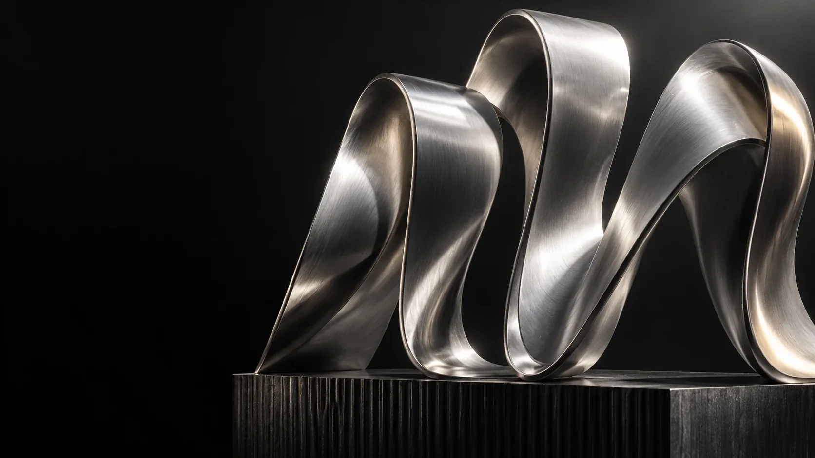 A flowing silver sculpture on a dark architectural plinth